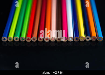 Matite multicolore su uno sfondo nero sono disposti in linea Foto Stock