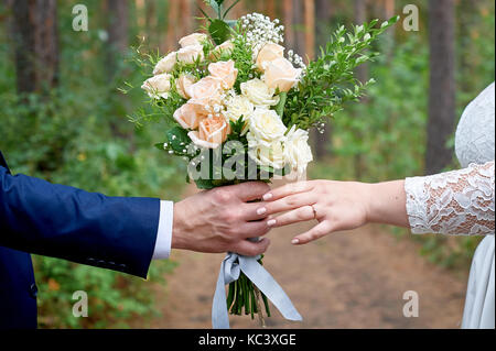 Sposo dà la sposa un bouquet di nozze per una passeggiata nel parco Foto Stock