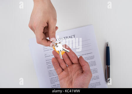 Immagine ritagliata di mano di dare le chiavi di casa al cliente con contratto carta sulla scrivania Foto Stock