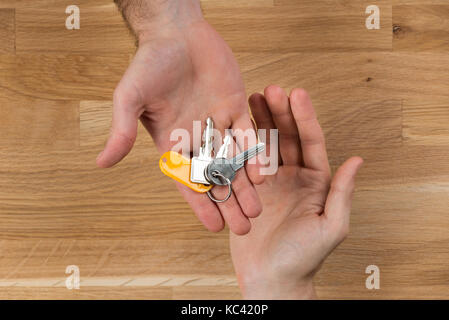 Immagine ritagliata di mano di dare le chiavi di casa al client alla scrivania in legno Foto Stock