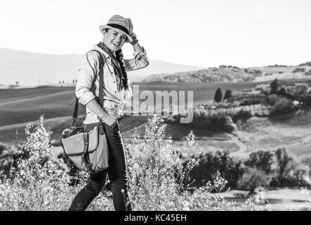 Alla scoperta di magiche vedute della Toscana. ritratto di sorridente donna attiva escursionista in hat godendo di vista in toscana Foto Stock