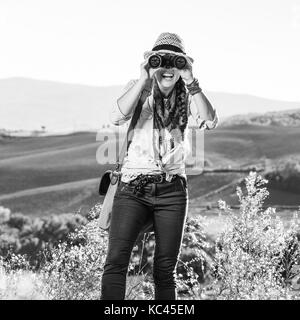 Alla scoperta di magiche vedute della Toscana. adventure donna escursionista in hat godendo la toscana vista guardando nella telecamera attraverso il binocolo Foto Stock