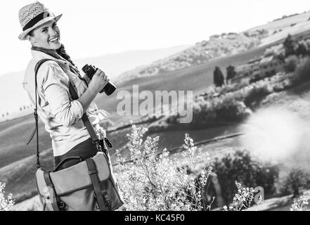 Alla scoperta di magiche vedute della Toscana. sorridente donna avventura escursionista in hat escursioni in Toscana con un binocolo Foto Stock