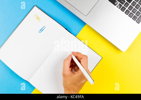 La donna la scrittura a mano in notebook su blu e sfondo giallo. vista superiore Foto Stock
