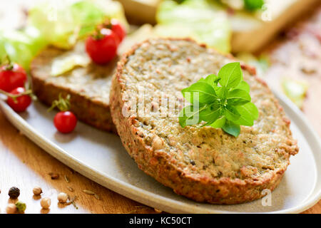 Primo piano di alcuni veggie hamburger di melanzane e altre verdure in una piastra, posto su una tavola in legno rustico Foto Stock