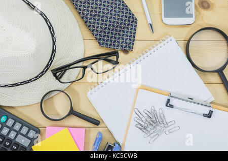 Tabella ufficio vista superiore con gli occhiali, nota prenota, lente di ingrandimento e il telefono cellulare sulla scrivania ingombra. ingombra scrivania da ufficio sfondo. Foto Stock