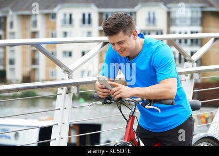 Giovane uomo utilizzando il telefono cellulare mentre fuori il giro in bicicletta nel contesto urbano Foto Stock