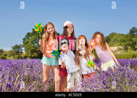 Felice preteen ragazze e ragazzi giocare con pinwheels nel campo di lavanda Foto Stock