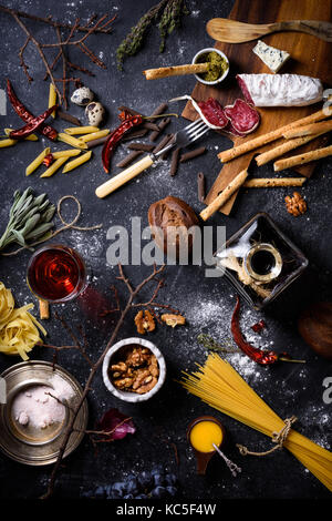 Antipasto, cucina italiana ingredienti pasta con antipasti, formaggio, grissini, spaghetti e vino su sfondo scuro. tabella vista dall'alto, Foto Stock