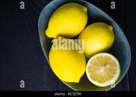 Freschi limoni organico in un giallo brillante coppa in ceramica su sfondo scuro Foto Stock