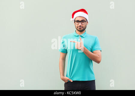 Imprenditore copia di puntamento spazio. uomo bello con la barba in maglietta blu guardando la fotocamera e rivolto lontano mentre in piedi isolato su sfondo grigio. Foto Stock