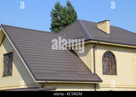 Casa del mattone giallo e marrone e tetto ondulato in metallo. tralicci su windows Foto Stock