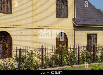 Casa del mattone giallo e marrone e tetto ondulato in metallo. tralicci su windows Foto Stock