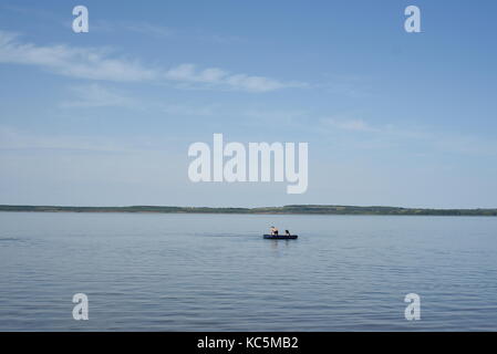 Due bambini vela su una barca in estate su un chiaro lago calmo e cielo blu Foto Stock