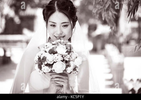 Bella e felice di giovani asiatici sposa che indossa abiti da sposa tenendo un mazzo di fiori in bianco e nero. Foto Stock