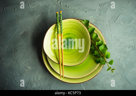 Tavolo rustico con impostazione vintage di piastre in ceramica, bacchette asiatici ed il ramo di edera impianto su dark vecchio tavolo in legno con copyspace Foto Stock