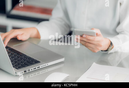 Close up imprenditrice tenendo il telefono cellulare e utilizzando computer laptop sulla scrivania in ufficio,business concetto di comunicazione. Foto Stock