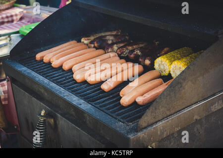 Salsiccia fresca. hot dogs grigliare all'aperto su un barbecue a gas grill con verdure melanzane con mais e patate Foto Stock