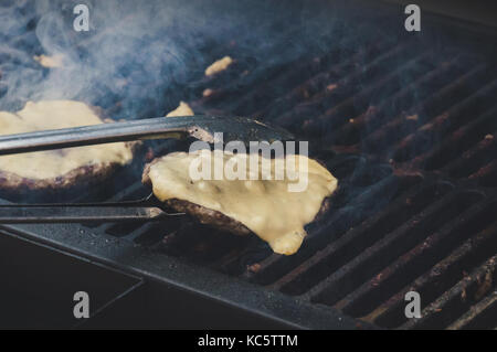 Grigliate di carne hamburger con il formaggio sulla parte superiore e di verdure sulla griglia fiammeggianti. Il formaggio fonde a caldo al patty sul grill. chef capovolge hamburger con met Foto Stock