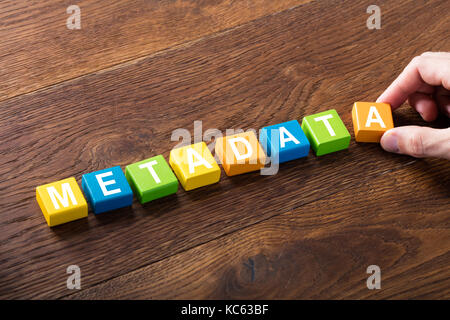 Angolo di alta vista di una persona con il concetto di metadati sul blocco colorato a scrivania in legno Foto Stock