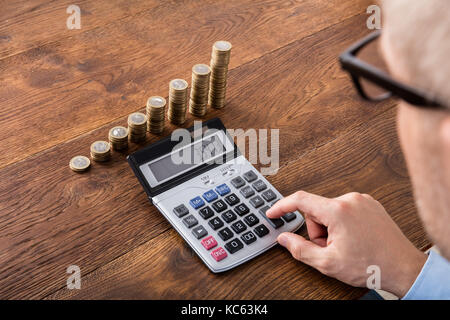 Persona mano facendo il calcolo sul bottone impilato e piggybank alla scrivania di legno. imposta sul reddito concetto Foto Stock