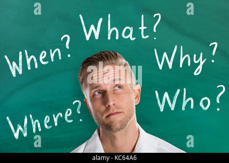 Giovane uomo pensando a cinque domande ws contro la lavagna Foto Stock