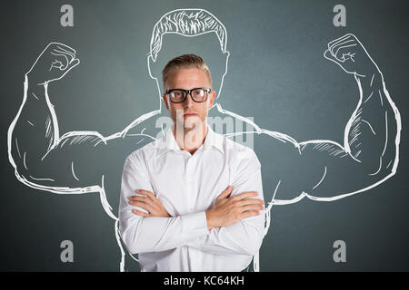 Conceptual giovane imprenditore in piedi di fronte a uno sfondo grigio con i muscoli del braccio di prelievo Foto Stock