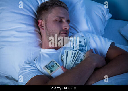 Uomo dorme sul letto con fascio di moneta note Foto Stock