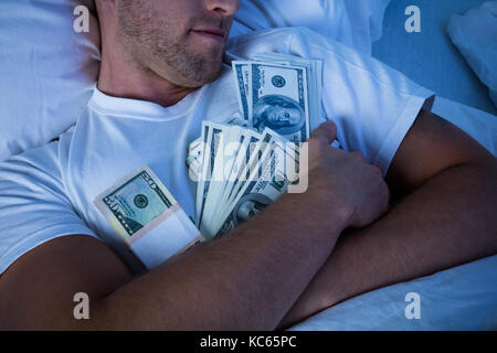 Uomo dorme sul letto con fascio di moneta note Foto Stock