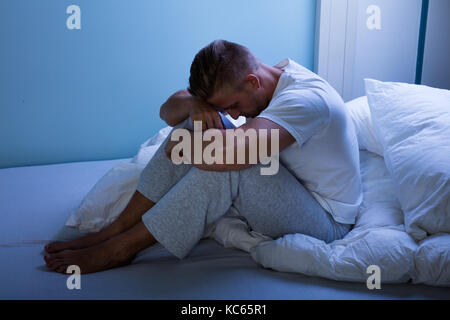 Triste giovane uomo seduto in pigiama sul letto Foto Stock