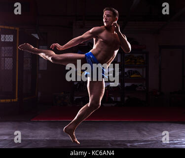 Un maschio di MMA fighter training calci e pugni in una palestra scuro Foto Stock