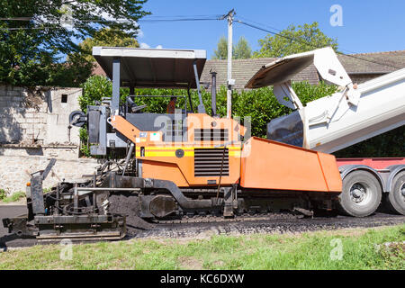 Punta di riempimento del carrello una strada tarring macchina con premix asfalto che si muovono lungo una molto stretta villaggio rurale street in unisono tarring la strada Foto Stock