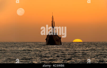 Ocean sunset nave silhouette è una vecchia nave di legno seduta in mare guardando il tramonto sull'oceano orizzonte. Foto Stock