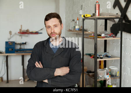 Ritratto di giovane serio tuttofare in piedi nella propria officina inte Foto Stock