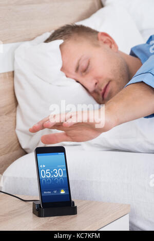 Uomo disteso sul letto del posticipo allarme sul display del cellulare Foto Stock