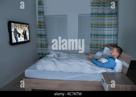 Foto di un uomo sdraiato sul letto a guardare la televisione Foto Stock