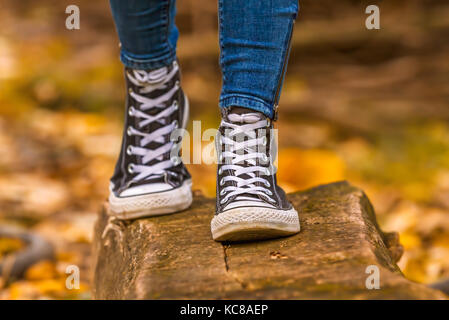 Ragazza indossa con nero sneakers camminando sul legno più cadono le foglie in autunno. Foto Stock