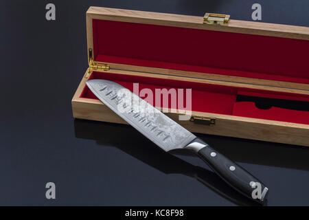 Santoku vegetali coltello da cucina con un elegante cofanetto in legno nero sulla superficie riflettente Foto Stock