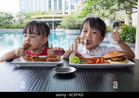 Asian poco ragazze cinesi di mangiare hamburger e pollo fritto a outdoor cafe Foto Stock