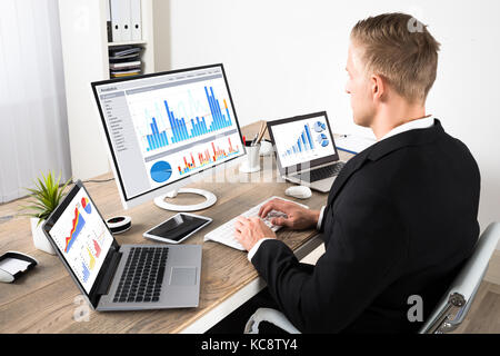 Giovane imprenditore analizzando su grafici su computer con tavoletta digitale e il computer portatile in ufficio Foto Stock