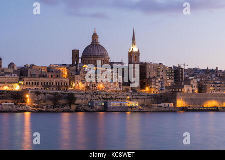 Bella guglie e cupola della cattedrale di la Valletta skyline sotto il blu cielo notturno, luci riflesse nell'oceano bay, La Valletta, la città capitale di Malta Foto Stock