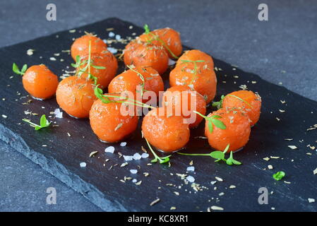 Glassato al miele carotine con sale marino e il timo su un grigio Sfondo astratto. Il mangiare sano concetto. fissaggio di cibo. pasto sano Foto Stock