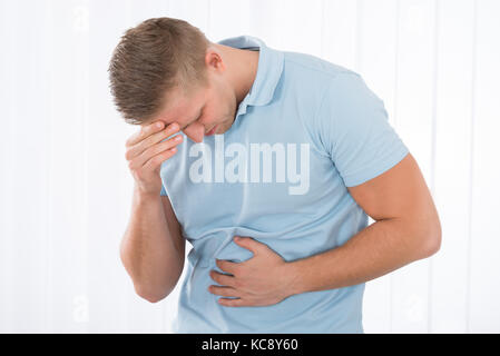 Giovane uomo che soffre di mal di stomaco in piedi a casa Foto Stock
