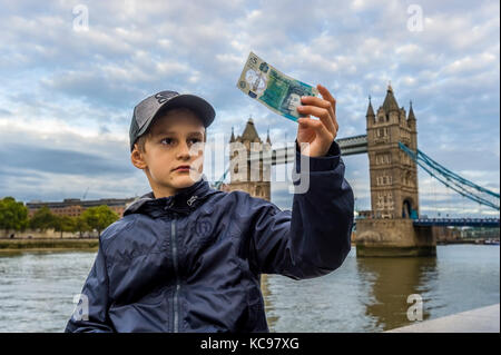 Ragazzo in berretto da baseball holding e guardando a new british 5 pound banconota Foto Stock
