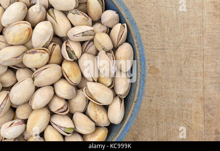 Top vista ravvicinata di un recipiente di ceramica riempito con arrosti di pistacchi di Bronte su un vecchio tavolo usurato. Foto Stock