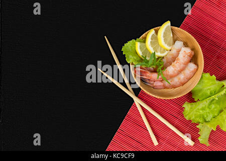 Cuocere i gamberi decorticati con le fette di limone, insalata verde e foglie di rucola su un piatto di legno con bacchette di legno incrociate. La piastra, bacchette e Foto Stock