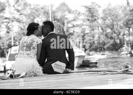 Giovane sposa e lo sposo seduta sul molo in legno kissing Foto Stock