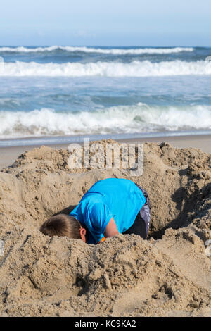 Avon, Outer Banks, North Carolina, Stati Uniti d'America. Ragazzo di scavare un buco nella sabbia. Foto Stock