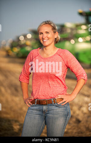 Un giovane agricoltore femmina sorge in un campo vicino a John Deere per le mietitrebbie precedenti per la mietitura del frumento sulla famiglia agriturismo vicino a Breckenridge, NORTH DAKOTA Foto Stock