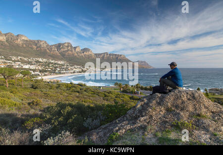 Uomo seduto sulla roccia a Camps Bay, Città del Capo, Western Cape, Sud Africa Foto Stock